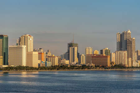 Manila, Philippines - March 5, 2019: South Harbor evening twilight shines on tall buildings, some under construction, south of Rizal Park under light blue sky behind dark blue sea water.のeditorial素材