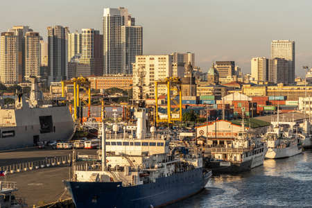 Manila, Philippines - March 5, 2019: South Harbor evening twilight shines on Philipine Coast Guard  dock and ships. Tall buildings in back. Vehicles and Shipping containers on pier.のeditorial素材