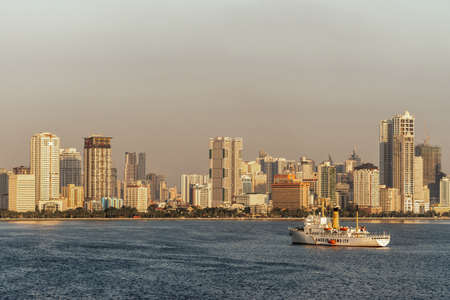 Manila, Philippines - March 5, 2019: South Harbor evening twilight shines on tall buildings such as Eton and Birch tower with Amosup rescue ships on dark blue sea water.のeditorial素材
