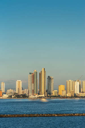Manila, Philippines - March 5, 2019: South Harbor evening twilight shines on portrait of tall buildings south of port. Ligh blue sky, dark blue sea water with breakwater.のeditorial素材