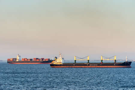 Manila, Philippines - March 5, 2019: Evening twilight shines on black and red Newark container ship and Pola Elisaveta general cargo ship sailing into South Harbor. Darker blue sea water.のeditorial素材