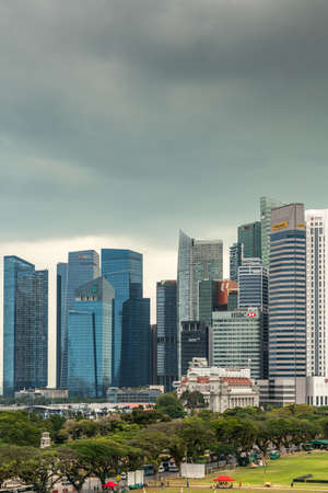 Singapore - March 20, 2019: Partial portrait of financial district skyscrapers from bay to Bank of China under dark gray cloudscape. Part of Padang, field of Cricket Club in front.のeditorial素材