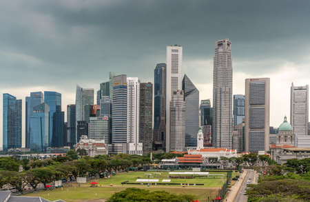 Singapore - March 20, 2019: Line of financial district skyscrapers from bay to Singtel building under dark gray cloudscape. Victoria theatre, National Gallery dome and Cricket Club in front.