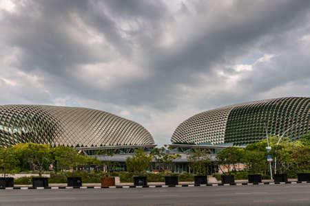 Singapore - March 20, 2019: Double Esplanade Theatres domes under heavy cloudscape. Shot with entrance to both in center. Fronted by Esplanade Drive and green tree foliage.のeditorial素材