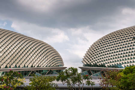 Singapore - March 20, 2019: Closeup of Double Esplanade Theatres domes under heavy cloudscape. Shot with entrance to both in center. Fronted by green tree foliage.のeditorial素材