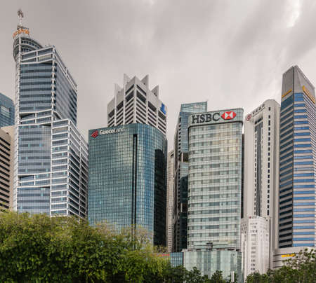 Singapore - March 20, 2019: Standing at Clifford Square looking towards a few financial district skyscrapers against dark  sky peeping over green foliage.のeditorial素材