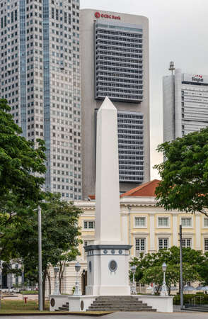 Singapore - March 20, 2019: White tall Dalhousie Obelisk on pedestal in front of skyscrapers of Financial District. Some green foliage at the fringes.のeditorial素材