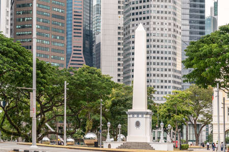 Singapore - March 20, 2019: White tall Dalhousie Obelisk on pedestal in front of skyscrapers of Financial District. Some green foliage at the fringes, and people walking by.のeditorial素材
