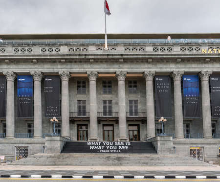 Singapore - March 20, 2019: What You See Is What You See, slogan, painted in white on steps of gray stone National Gallery. Flag on top under gray sky. Color added by a few banners.のeditorial素材