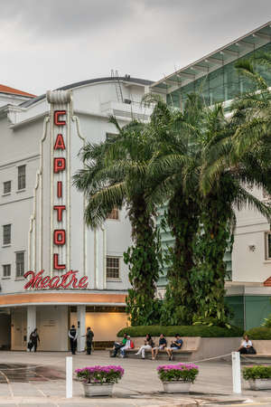 Singapore - March 20, 2019: Light gray facade with red neon sign naming Capital Theatres in street scene with people and green palm trees under gray sky.のeditorial素材