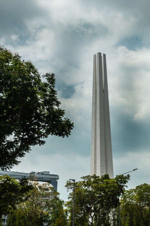 Singapore - March 20, 2019: Beige tall war memorial obelisk towering over green foliage of War Memorial Park under blue sky with plenty of white clouds.のeditorial素材
