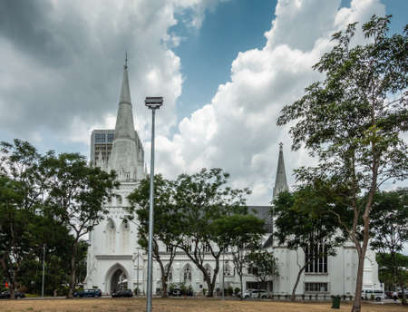 Singapore - March 20, 2019: White historic Saint Andrews Cathedral in its own park with dried lawn, green trees under blue sky with big white clouds. Cars parked and people.のeditorial素材