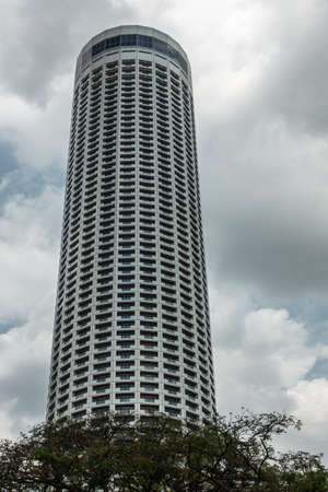 Singapore - March 20, 2019: Closeup of Tower of Swissotel The Stamford over green foliage and under heavy gray cloudscape.のeditorial素材
