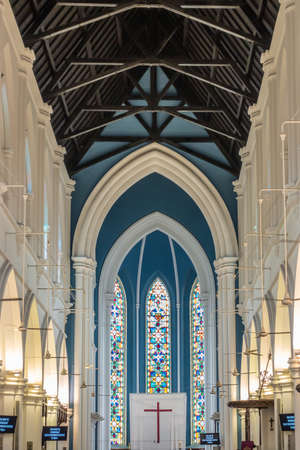 Singapore - March 20, 2019: Inside White historic Saint Andrews Cathedral. Dark brown wooden ceiling and white and blue walls with stained glass windows above nave and chancel.のeditorial素材