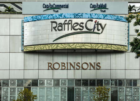 Singapore - March 20, 2019: Raffles City shopping mall entrance with signs displayed such as Robinsons and CapitaCommercial Trust. Some green foliage against gray facade.のeditorial素材
