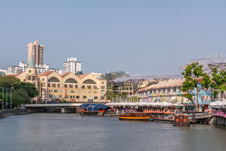 Singapore - March 21, 2019: Boats on Singapore River at North Boat Quay with its colorful houses, now bars and restaurants under blue sky. Read bridge and converted warehouses with tower.のeditorial素材