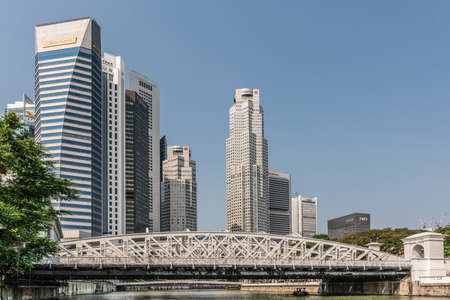Singapore - March 21, 2019: Along Singapore River. White Anderson bridge over river with skyscrapers of Financial District behind under blue sky.のeditorial素材