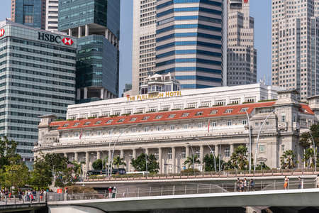 Singapore - March 21, 2019: On Marina waters. The Fullerton Hotel behind Esplanade road and Jubilee pedestrian bridge. Walls of financial district skyscrapers behind.のeditorial素材