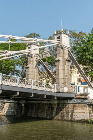 Singapore - March 21, 2019: From Singapore River. Closeup of white-gray north gate and pull mechanism of metal Cavenagh drawbridge. Green foliage in back.のeditorial素材