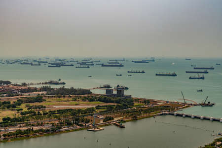 Singapore - March 21, 2019: Shot from Sands roof. Birds eye view on tens of ships anchored in Singapore Strait under silver hazy sky. Some coastal land and bay entrance up front.のeditorial素材