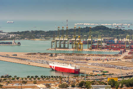 Singapore - March 21, 2019: Shot from Sands roof. Birds eye view on port with container terminal, car terminal and rows of white fuel tanks. Some green barrier and ships on Strait.のeditorial素材