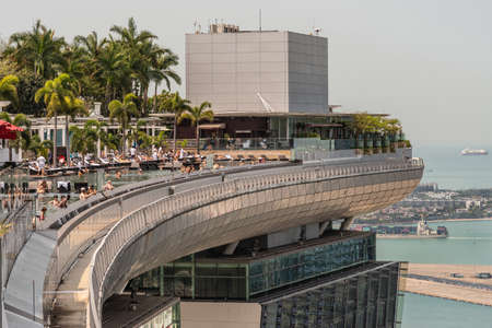 Singapore - March 21, 2019: Marina Bay Sands observation deck has a large swimming pool ares featuring also palm trees. Lots of people. Small Singapore Strait view and port area.のeditorial素材