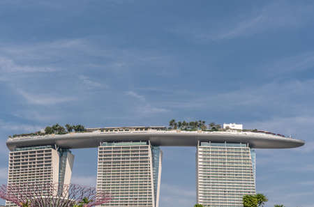 Singapore - March 22, 2019: At Gardens by the Bay. View onto Marina Bay Sands hotel and casino building against blue sky. Top of supertree.のeditorial素材