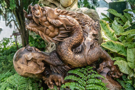 Singapore - March 22, 2019: Gardens by the Bay, the Cloud Forest Dome. Large brown wooden Chinese Style monster statue crawls through dense green vegetation.のeditorial素材