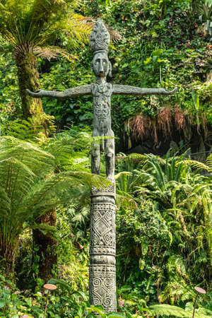 Singapore - March 22, 2019: Gardens by the Bay, the Cloud Forest Dome. Greenish wooden Totem pole with male figure on top in Maori style backed by a wall of green jungle vegetation.のeditorial素材