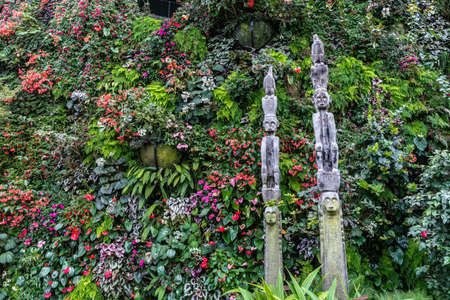 Singapore - March 22, 2019: Gardens by the Bay, the Cloud Forest Dome. Two Totem pole with figures of man and birds on top backed by a wall of green jungle vegetation and many flowers.のeditorial素材