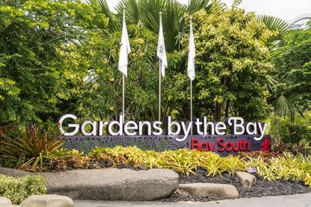 Singapore - March 22, 2019: Gardens by the Bay name as white, red and gray monument set under three white flags against green foliage and yellowish ground plants in front.のeditorial素材