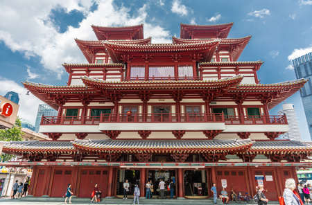 Singapore - March 22, 2019: Chinatown. Main entrance maroon-red facade of Buddha Tooth Relic Temple and Museum under blue sky with white clouds. People in front.のeditorial素材