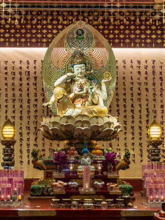 Singapore - March 22, 2019: Buddha Tooth Relic Temple in Chinatown. Closeup of crowned and multi-armed Lord Buddha sitting on lotus and showing chakra wheel. placed on altar with sanskrit letter background.のeditorial素材