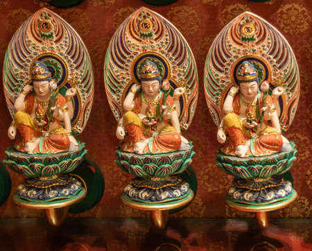 Singapore - March 22, 2019: Buddha Tooth Relic Temple in Chinatown. Closeup of three small Buddha statues on a wall of hundreds. He sits on lotus, has backdrop and reflects.のeditorial素材