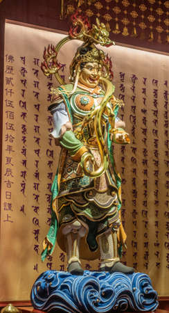 Singapore - March 22, 2019: Buddha Tooth Relic Temple in Chinatown. Closeup of tall colorful Dwarapalaka guardian on side of Buddha altar. Mandarin and Sanskrit figures in back.のeditorial素材