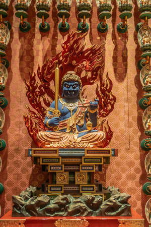 Singapore - March 22, 2019: Buddha Tooth Relic Temple in Chinatown. Closeup of blue Acala, guardian deity, statue sitting on altar, backed by red flames, holding sword. Orange dominant color.のeditorial素材