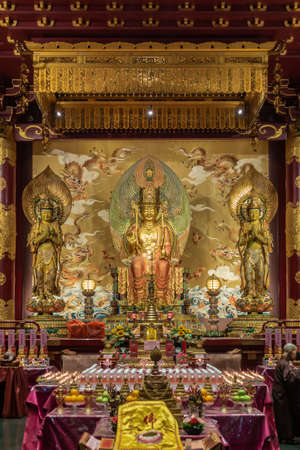 Singapore - March 22, 2019: Buddha Tooth Relic Temple in Chinatown. Longer shot on altar with 3 giant statues. Medicine Buddha in center, flanked by 2 Bothisattvas. Gold dominant. Sky, dragon reredos.のeditorial素材