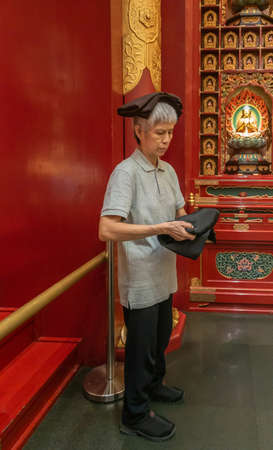 Singapore - March 22, 2019: Buddha Tooth Relic Temple in Chinatown. Female attendant distributes dark brown folded robes while carrying them on her head and in her hands.のeditorial素材