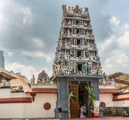 Singapore - March 22, 2019: Sri Mariamman Hindu Temple on South Bridge Road. main entrance with colorful Gopuram tower against dark cloudscape. Beige wall and tall brown door with people.のeditorial素材