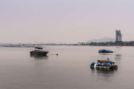 Si Racha, Thailand - March 16, 2019: Royal Thai Police boat and small fishing vessels on flat gray water just off beach of the town.  Tall building under construction on shore.のeditorial素材