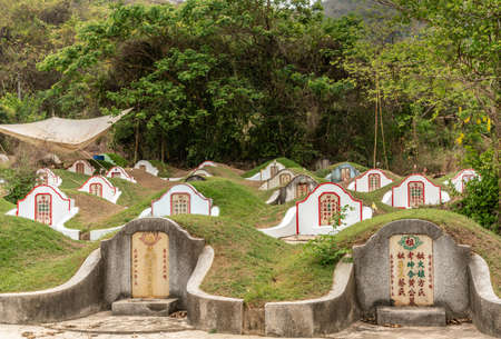 Bang Phra, Thailand - March 16, 2019: Chao Pho Khao Chalak Chinese Cemetery. Group of family graves with beige tombstone with colored Mandarin letters set against wall. Beige shade tarp overhead.のeditorial素材