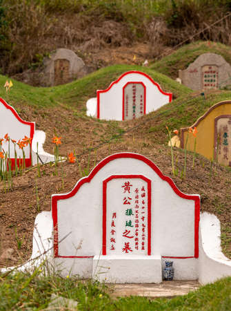 Bang Phra, Thailand - March 16, 2019: Chao Pho Khao Chalak Chinese Cemetery. Red on white family grave with more in back. Mandarin lettering, dirt hills and flowers.のeditorial素材