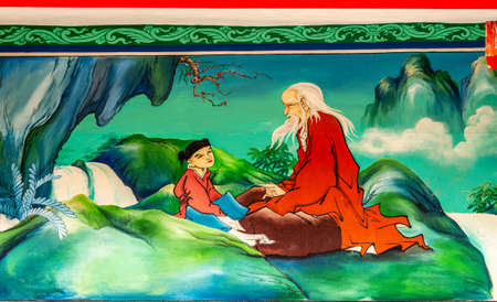 Bang Phra, Thailand - March 16, 2019: Chao Pho Khao Chalak Chinese Cemetery. Reunion hall and shrine for mourning families. Outer wall painting of older guru teaching boy in greenish landscape.のeditorial素材