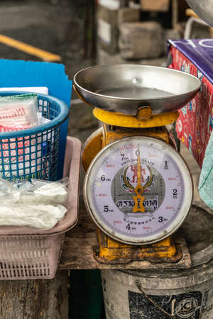Chon Buri, Thailand - March 16, 2019: Closeup of large table-top retailer scale on street market surrounded by baskets, bags and more on Sukhumvit Road.のeditorial素材