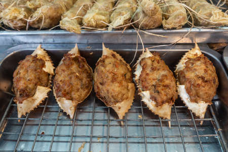 Chon Buri, Thailand - March 16, 2019: Nong Mon market. Closeup of five crab shells filled with prepared, cooked crab meat in dough on a metal grill sold in booth.の写真素材