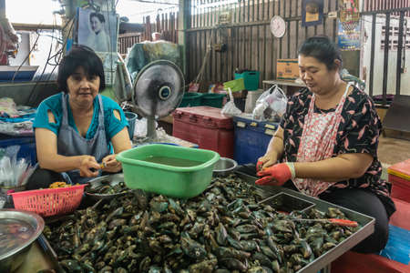 Chon Buri, Thailand - March 16, 2019: Nong Mon market. Two sitting women in front of pile of black mussels clean and open them. Chaotic scene with colroed baskets and basins.のeditorial素材