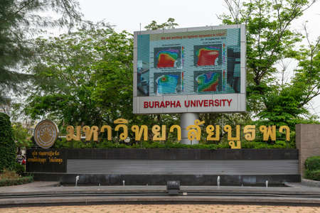 Chon Buri, Thailand - March 16, 2019: Large life video-screen and in gold spelled out name of Burapha University with logo and emble,  at Long-hard Bangsaen Road. Green foliage and silver sky.のeditorial素材