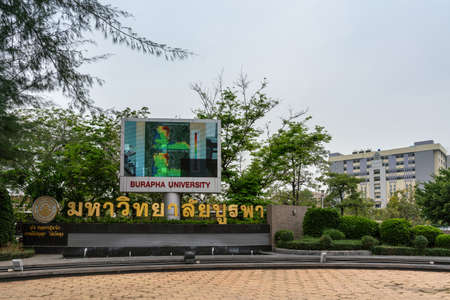 Chon Buri, Thailand - March 16, 2019: Large life video-screen and in gold spelled out name of Burapha University with logo and emble, and building at Long-hard Bangsaen Road. Green foliage and silver sky.のeditorial素材