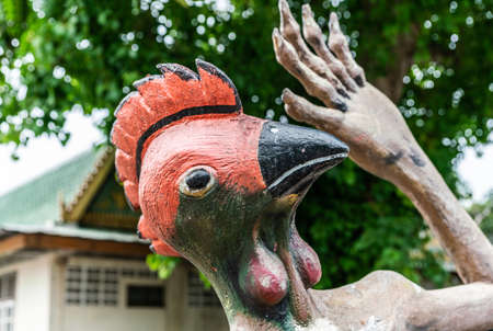 Bang Saen, Thailand - March 16, 2019: Garden of Hell in Wang Saensuk Buddhist Monastery. Closeup of head of chicken depicting a torturer against green foliage.の写真素材