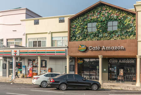 Chachoengsao, Thailand - March 17, 2019: Brown facade with green foliage and flowers labeled CafÃ© Amazon, a coffee house along Motorway 7. White 7-eleven retail store as neighbor. Light blue sky.のeditorial素材